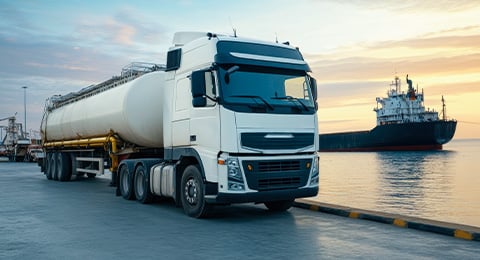 tanker truck on road next to a ship on water
